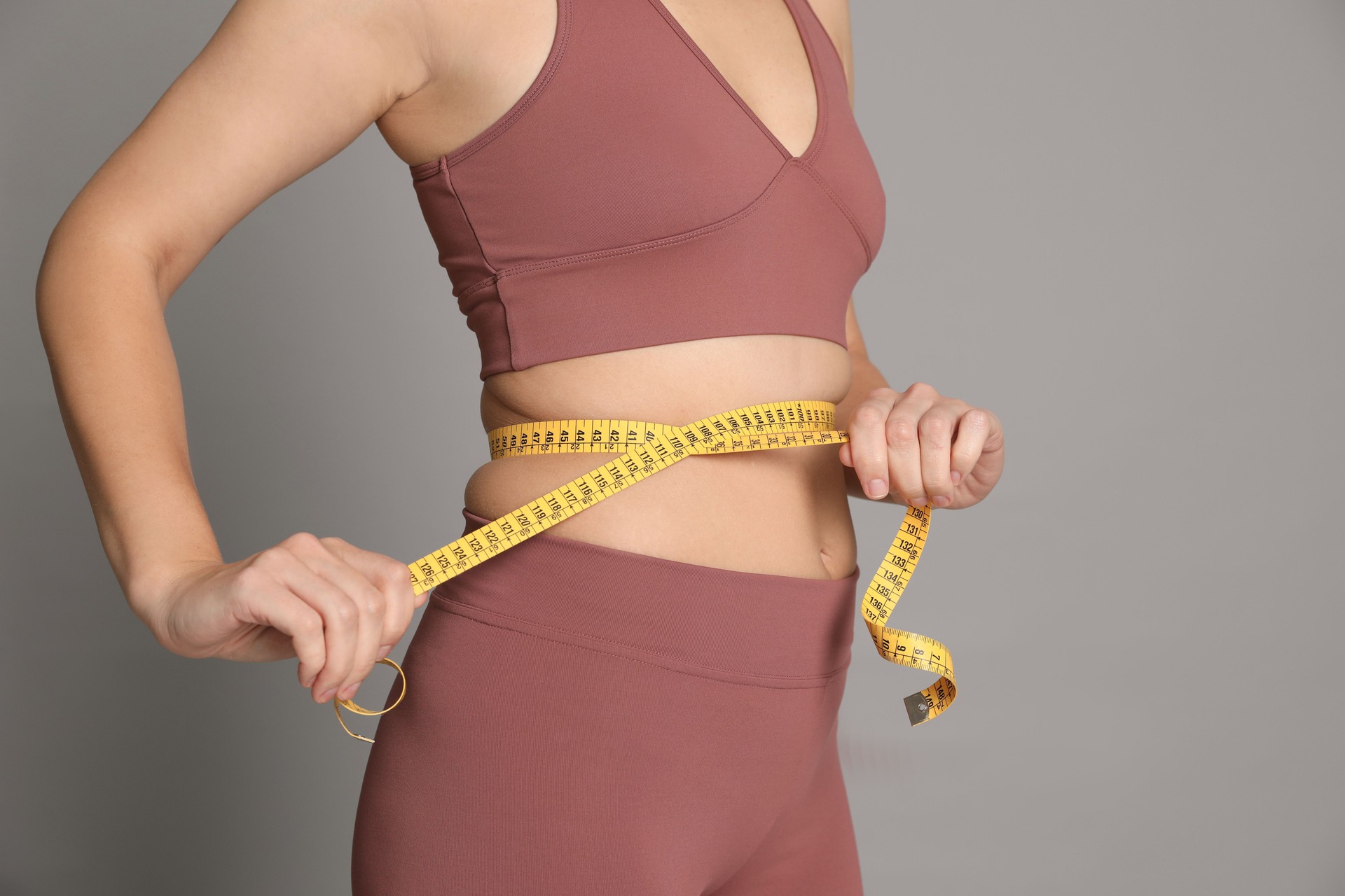 Woman measuring waist with tape on grey background, closeup Woman measuring waist with tape on grey background, closeup
